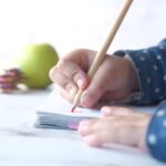 Close up of a child hand drawing with colored pencil on a page.