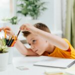 Distance learning online education. Caucasian smile kid boy studying at home with book, draw in