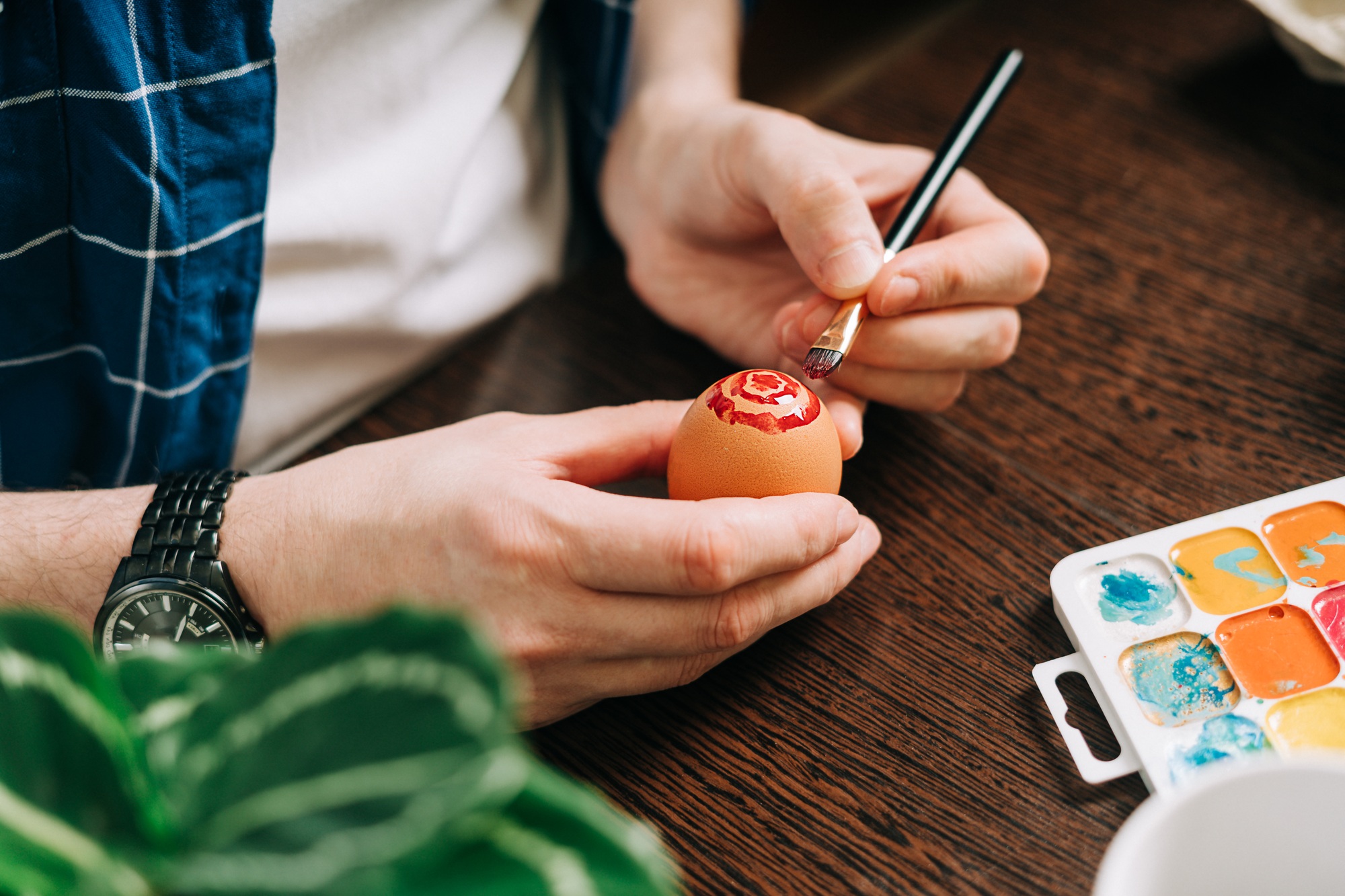 Easter day. Cropped hands of Adult man painting eggs on wooden background. Sitting in a kitchen with