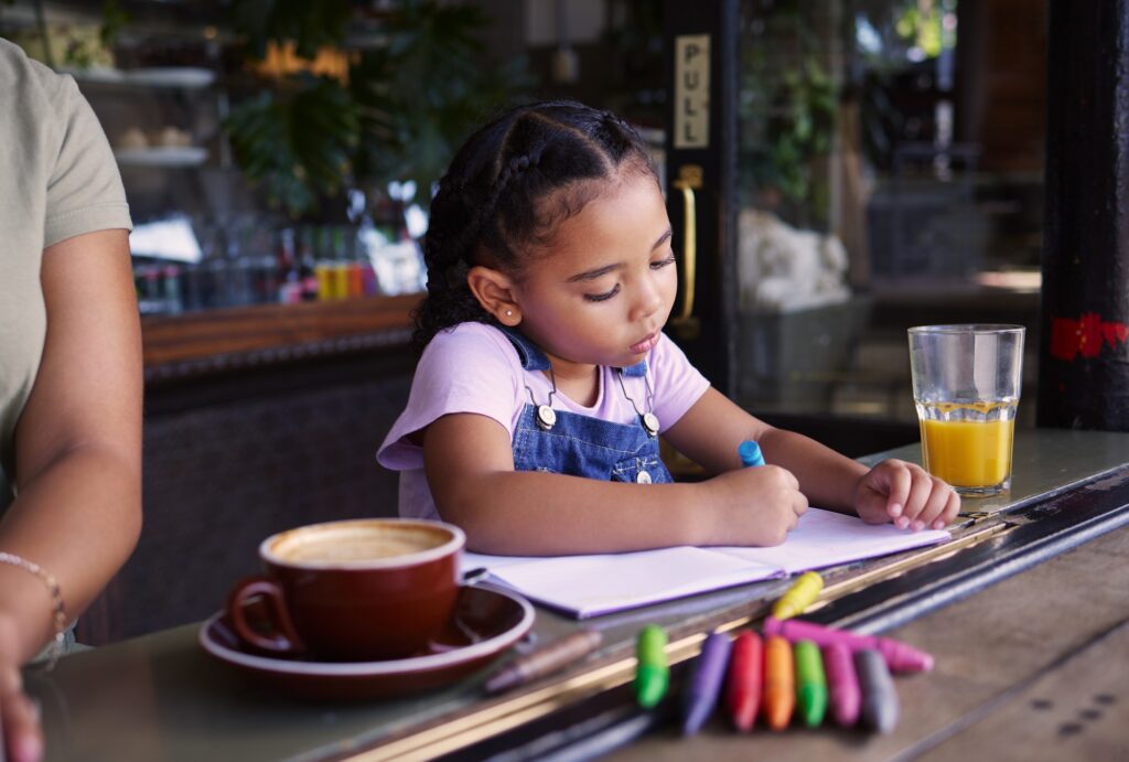 Girl child color in book at cafe, creative and drawing with crayons, family day to relax with learn