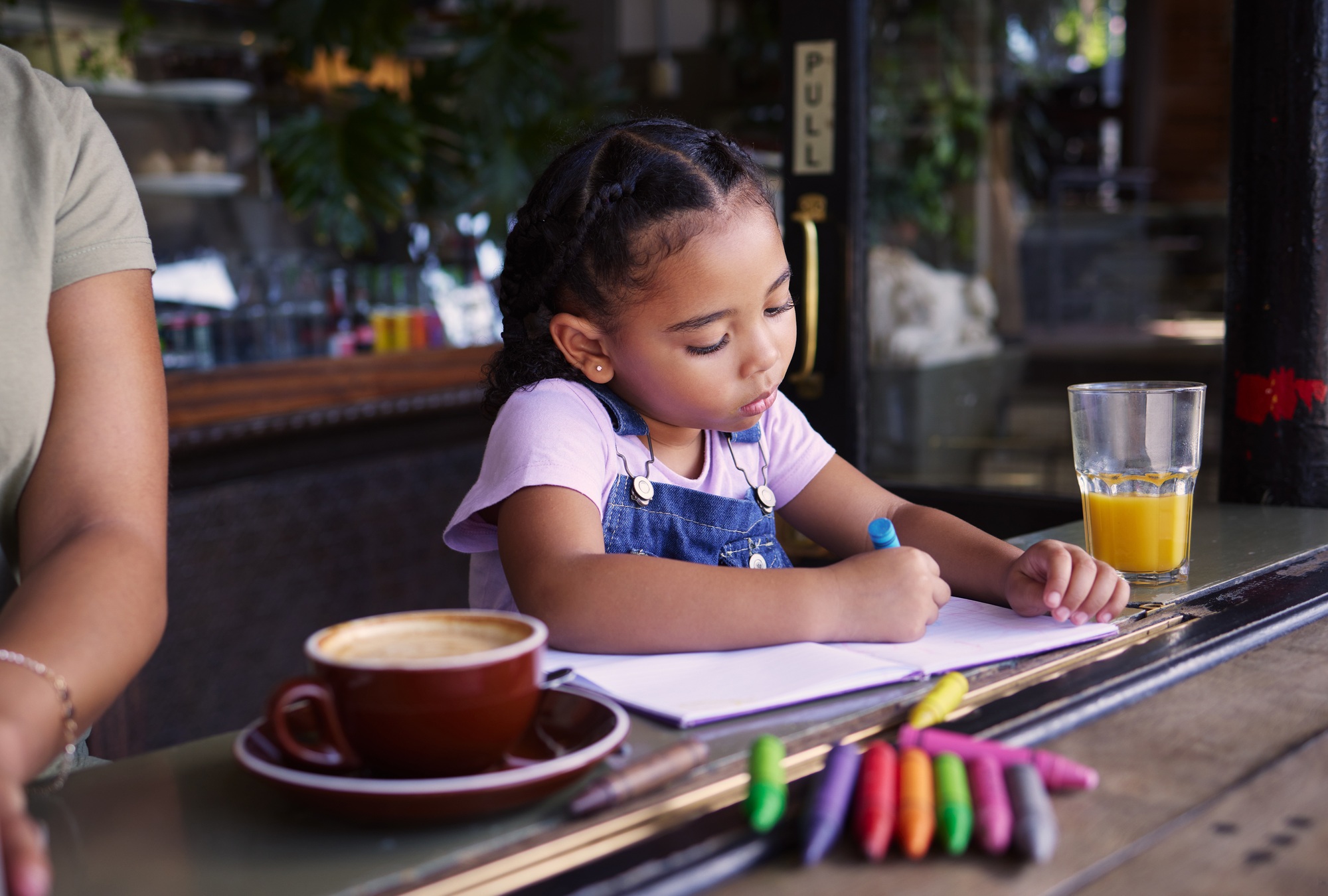 Girl child color in book at cafe, creative and drawing with crayons, family day to relax with learn