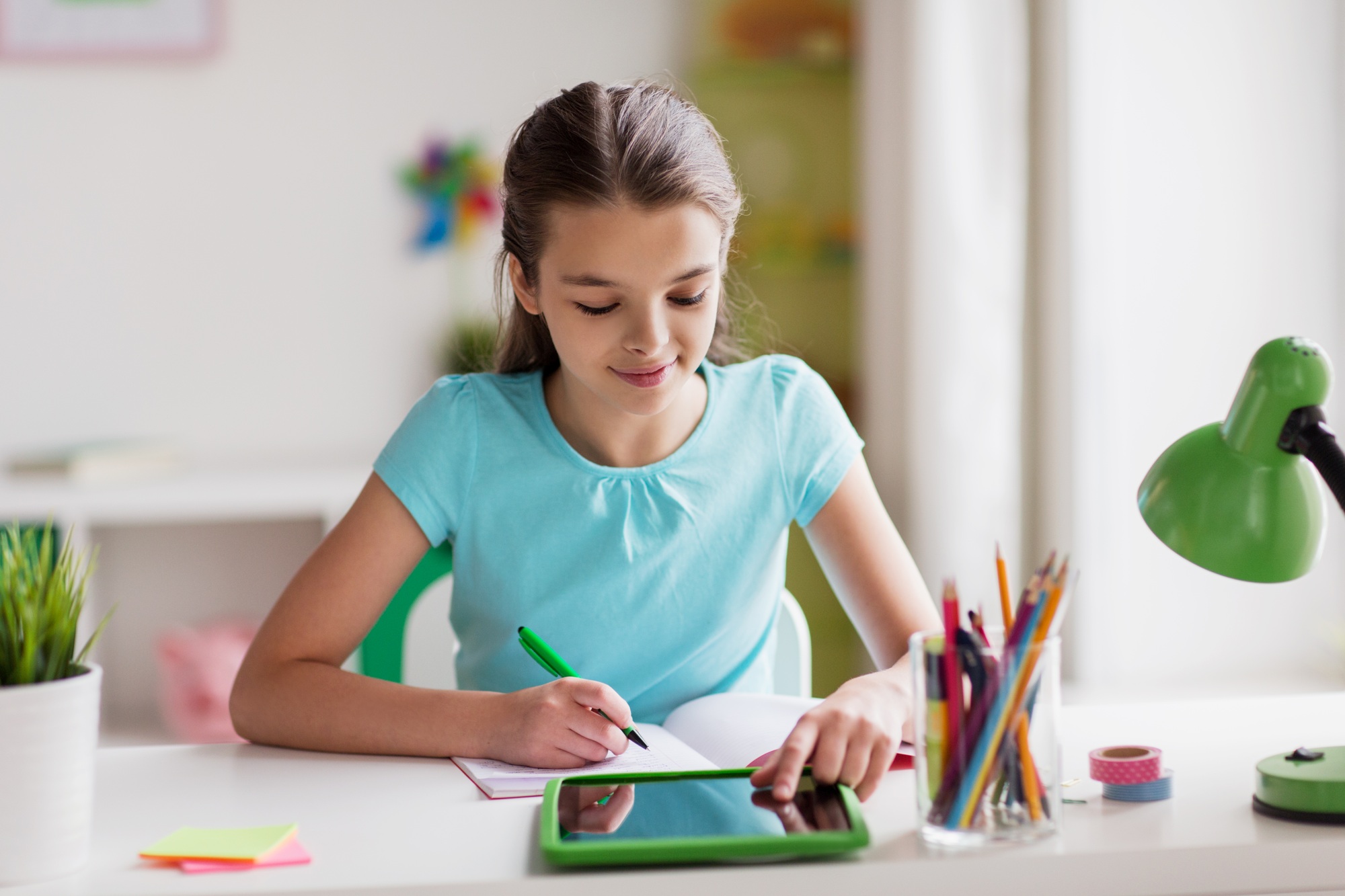 girl with tablet pc writing to notebook at home