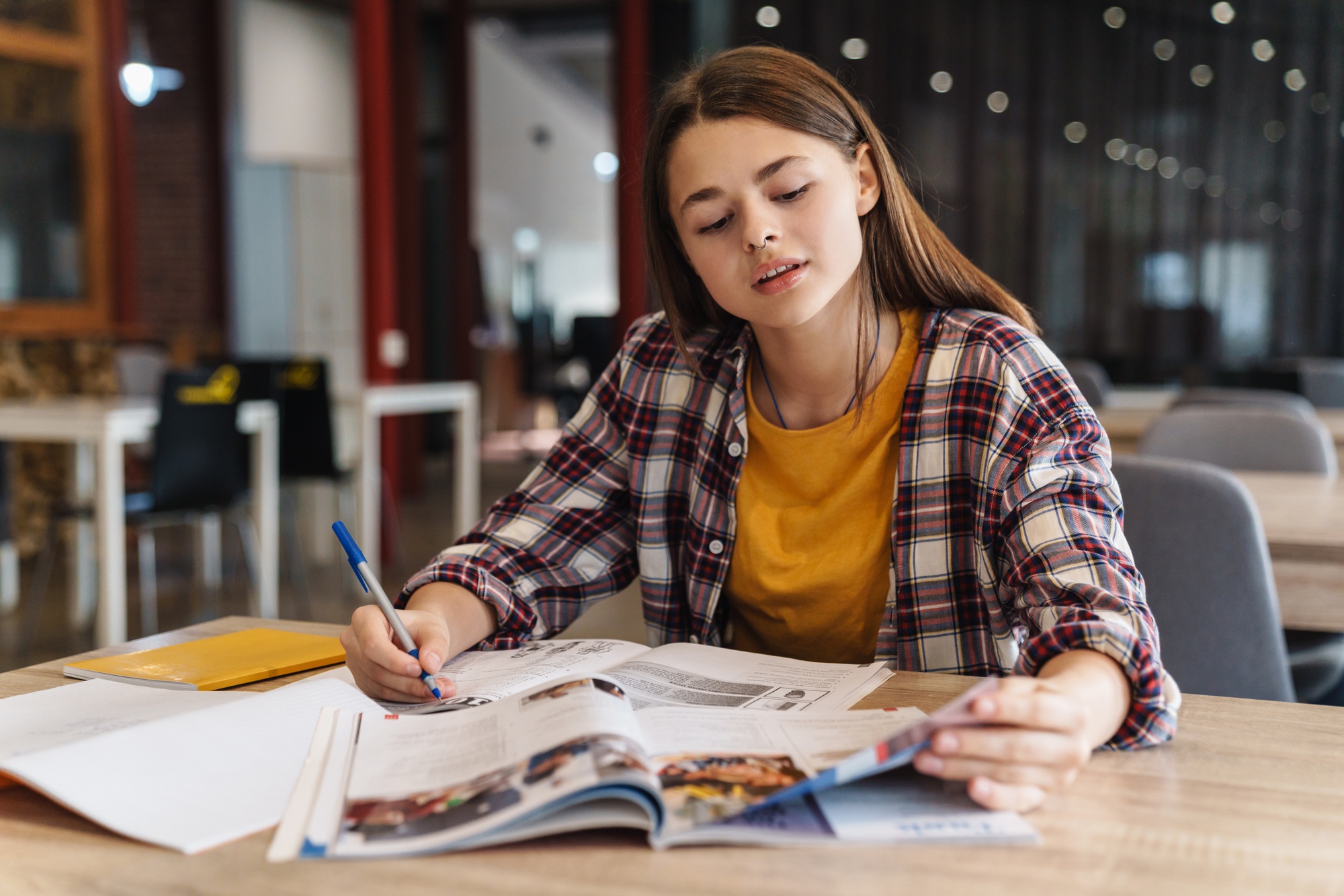 Image of serious caucasian girl doing homework with exercise books