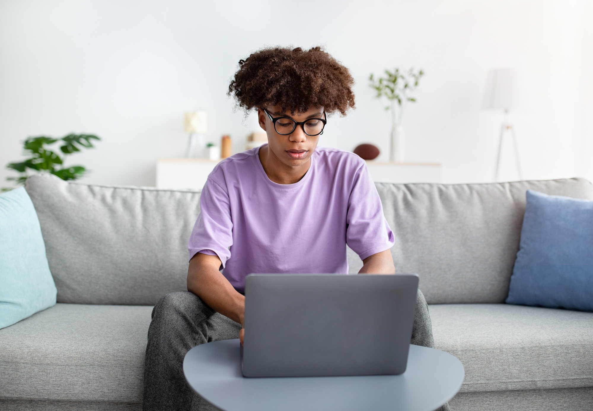 Intelligent black teen guy studying remotely from home, uing laptop pc, writing online test