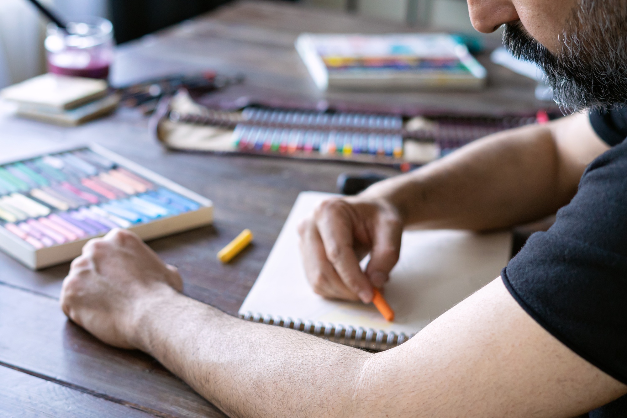 man painting with color pencil and pastel crayon chalks on paper. box color pencils