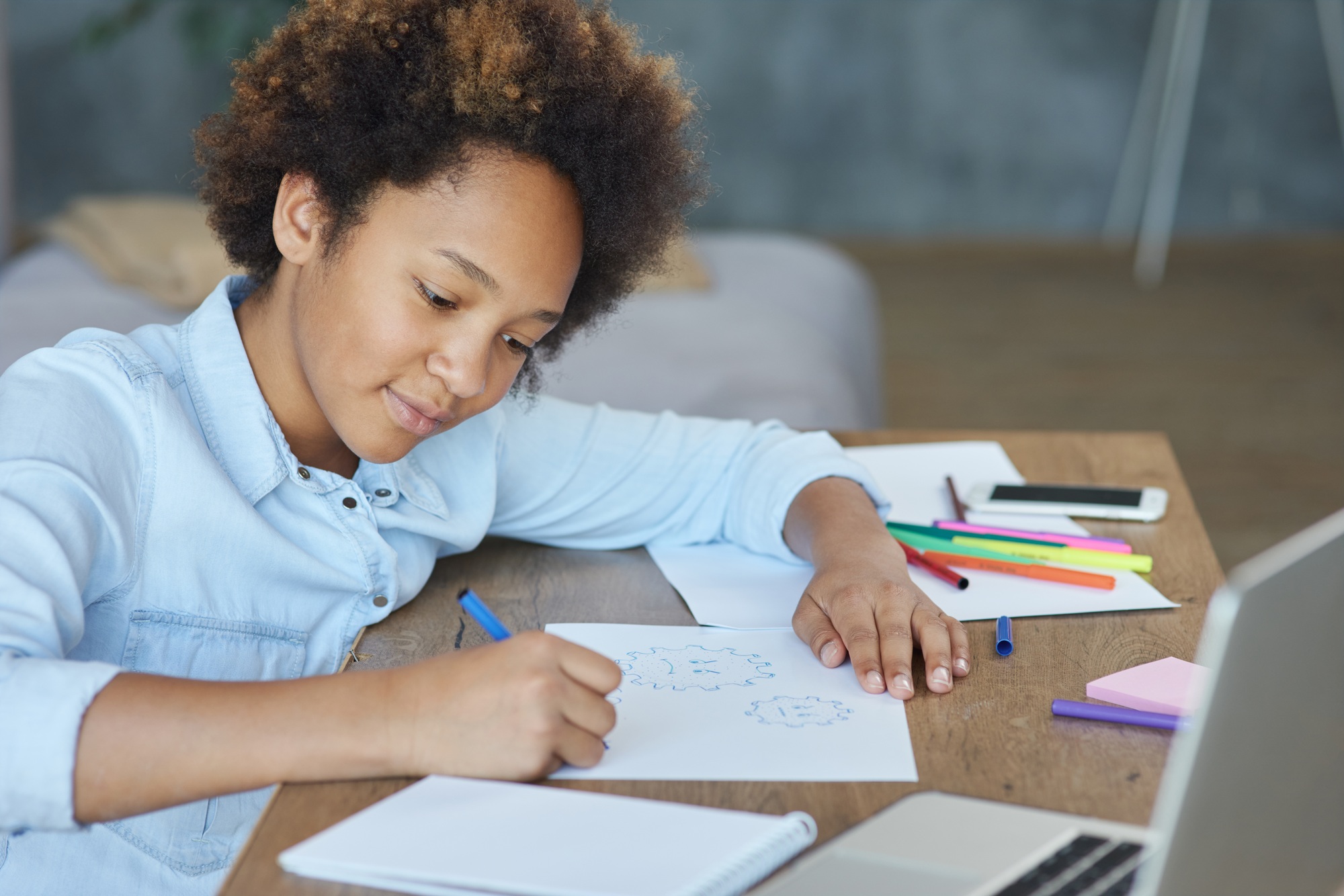 Mixed race teen schoolgirl looking focused while drawing on paper with colorful markers, spending