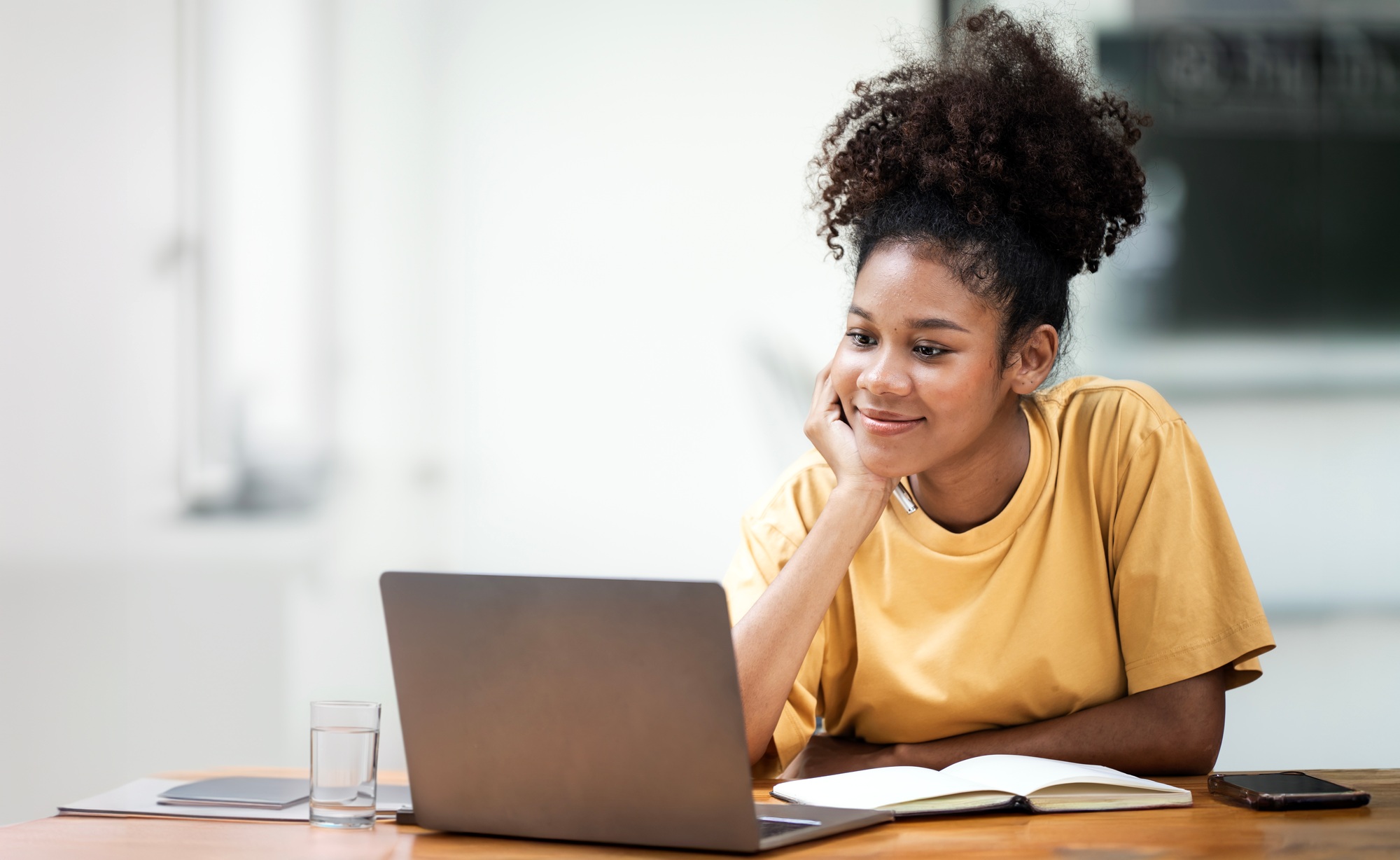 Smiling young black woman student sitting at desk watching on laptop. Happy female studying using pc