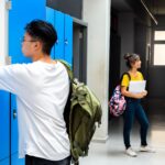 Teen asian high school student putting books away in lockers. Teenagers talking in school corridor.