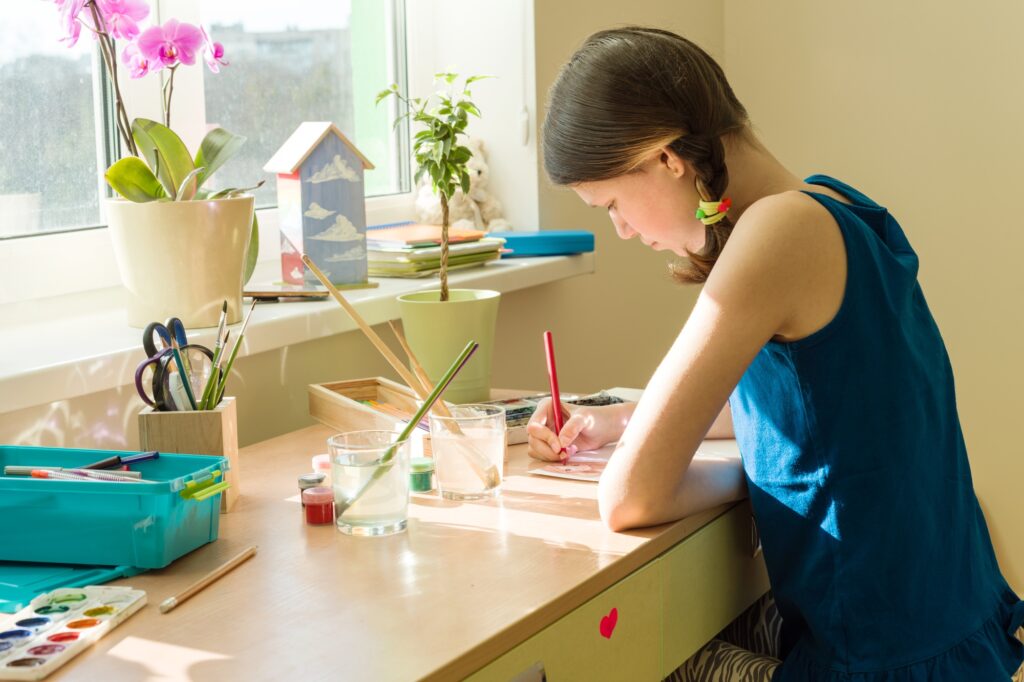 Teenage girl at home is engaged in creativity, draws watercolor at a table in room