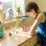 Teenage girl at home is engaged in creativity, draws watercolor at a table in room