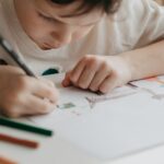 The boy draws with pencils at the kitchen